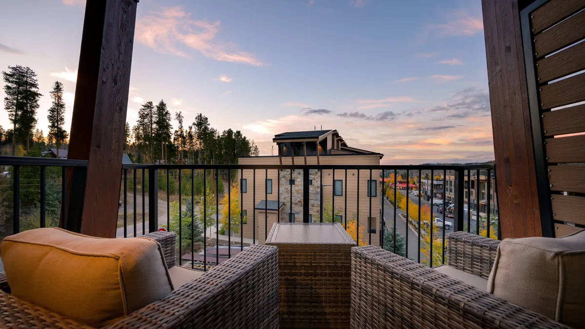 A tranquil balcony seating area overlooks distant trees and a colorful sunset sky, providing a perfect outdoor setting for relaxation and group conversations while being surrounded by nature.