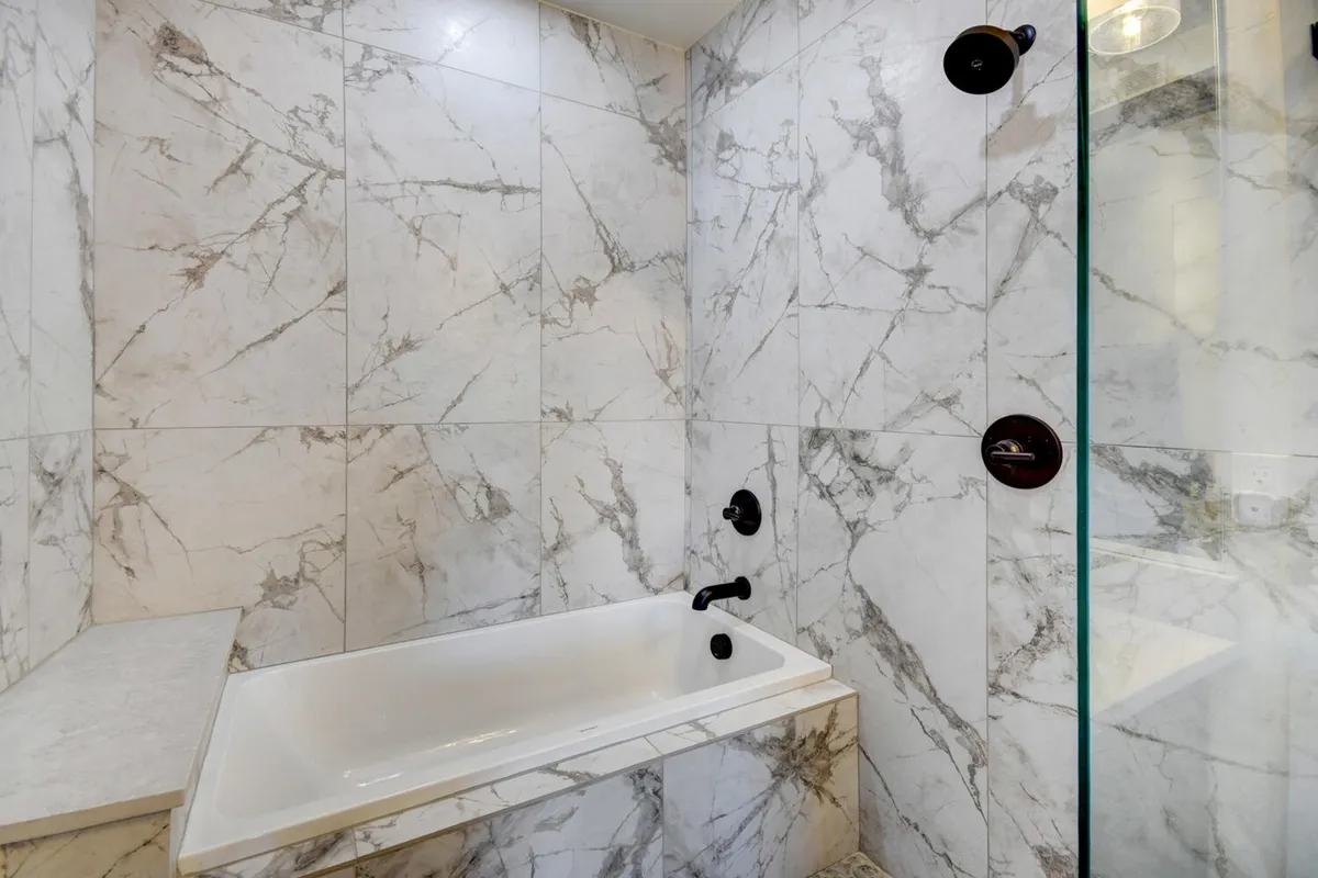 A spa-inspired bathroom with a sleek bathtub, marble walls, a separate shower area, and elegant black fixtures, radiating a sense of calm and luxury.