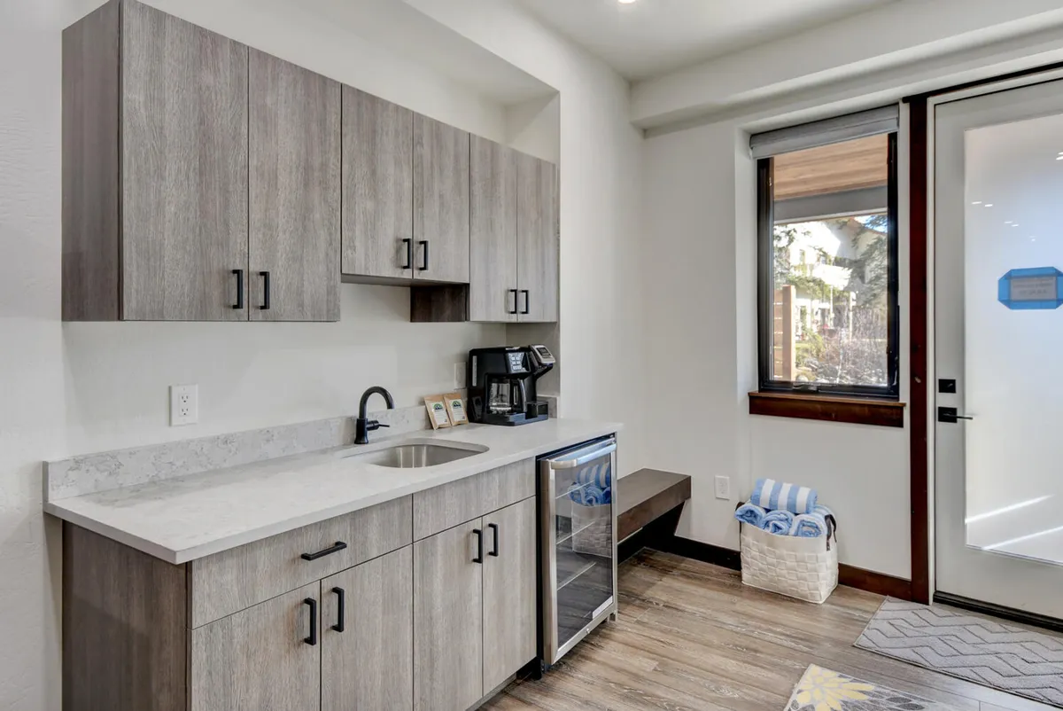 A kitchenette with a coffee maker, sink, refrigerator, and a window letting in natural light. The casual, welcoming mood is perfect for sipping craft coffee and informal gathering.