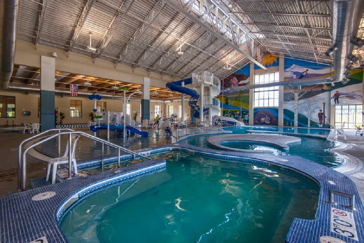 A lively indoor pool scene featuring water slides, a spacious swimming area, and a colorful mural. The setting is vibrant and family-friendly, inviting guests to enjoy aquatic fun and relaxation.