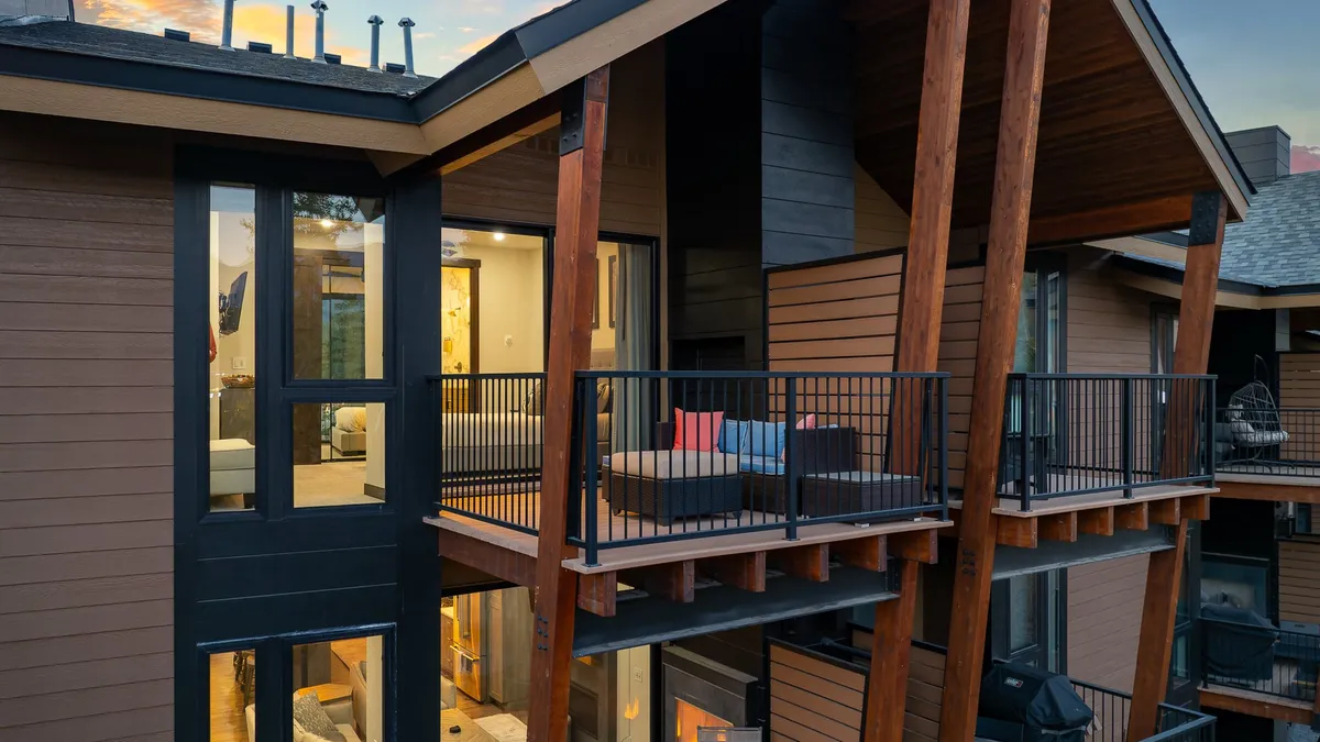 A cozy balcony is outfitted with plush seating and framed by wooden beams, providing sweeping views through large windows. The space is perfect for relaxing outdoors, entertaining guests, or enjoying sunset vistas over the mountains and creek below.