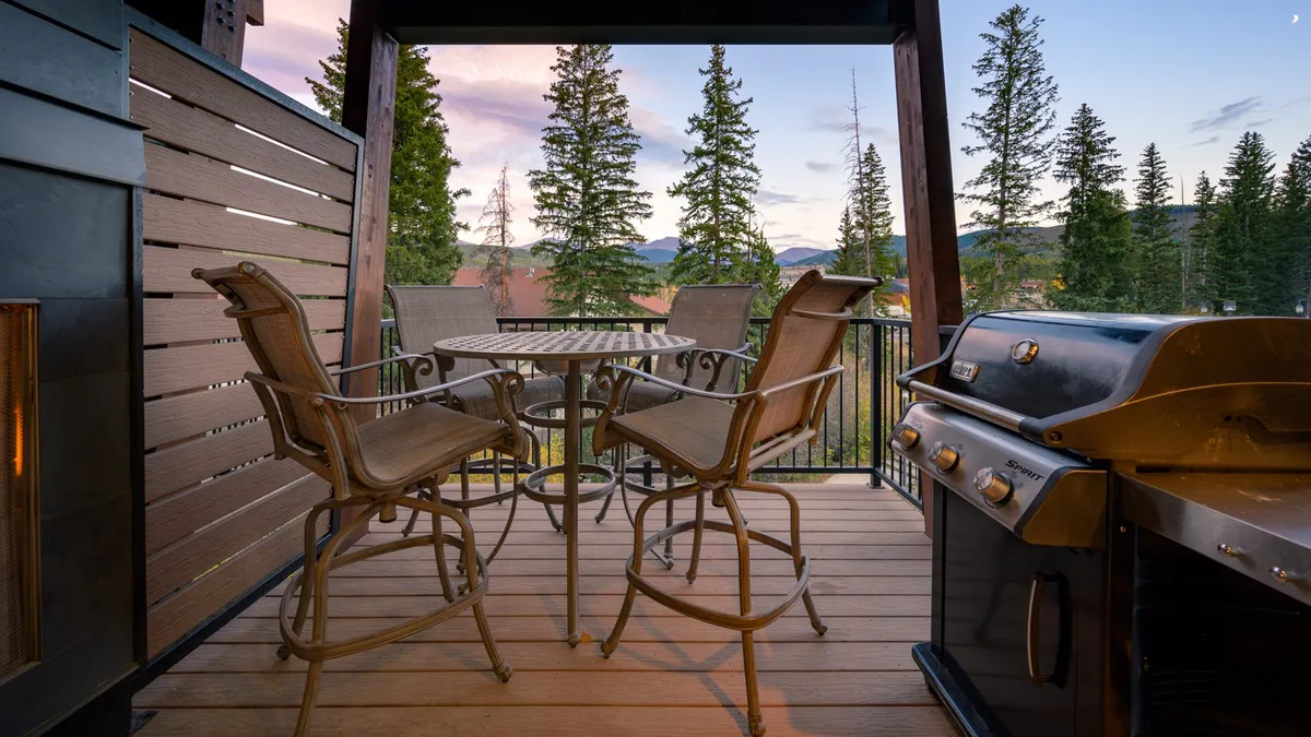 This exterior scene highlights a spacious outdoor area featuring comfortable seating and a grill, with the majestic mountains providing a picturesque backdrop. The setting encourages barbecuing, al fresco dining, and socializing as the sun sets.