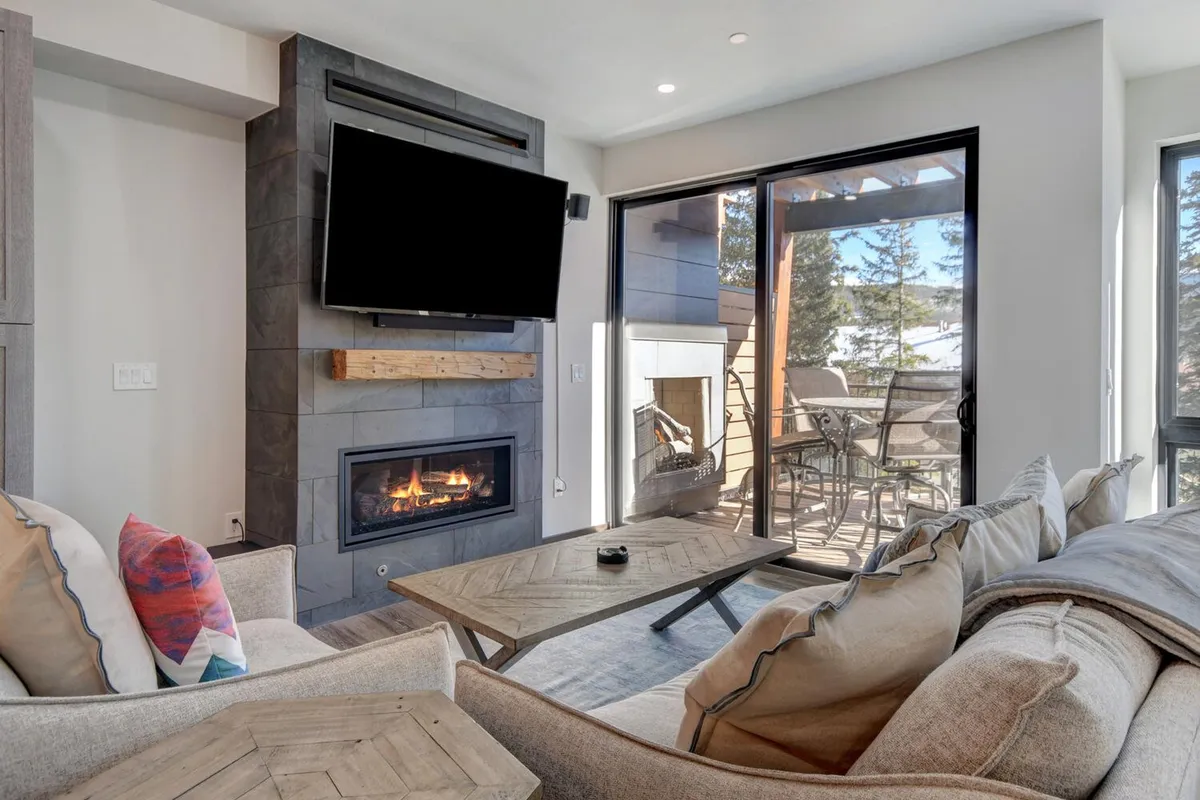 A warm, welcoming living room with plush seating, a contemporary gas fireplace, large windows, and a prominent television. The space feels perfect for relaxing after dinner, hosting board game nights, or enjoying a home theater experience in comfort.