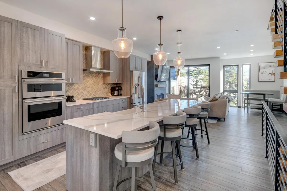 A luminous, open-concept kitchen with a large island at its center, surrounded by modern stainless-steel appliances and contemporary cabinetry. Expansive windows let in abundant natural light, and the open floor plan flows seamlessly into living and dining spaces, perfect for gatherings.