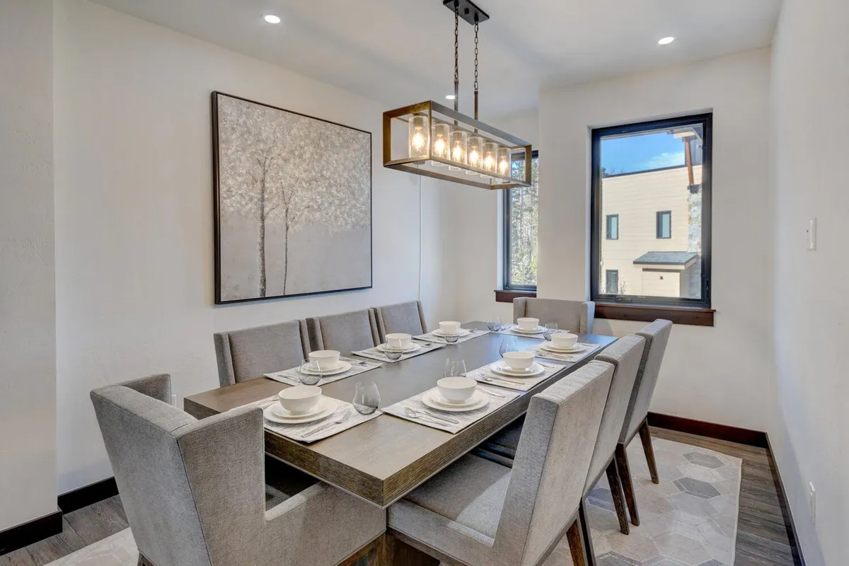 A generous dining area featuring a long table with elegant place settings, a modern chandelier overhead, and large windows bathing the space in light. The table offers seating for many, perfect for big family breakfasts or festive dinners as described in the section.