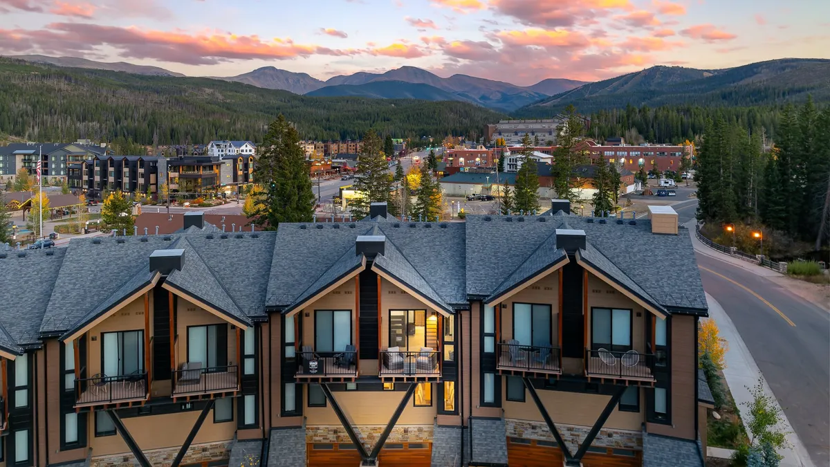 A tranquil mountain view from a balcony at sunset, overlooking a vibrant town below, with hints of people relaxing and pathways leading to outdoor explorations. This image ties the sense of place to the freedom and access guests have to both private relaxation and nearby adventures.